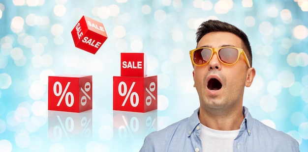 emotions, shopping, sale, discount and people concept - face of scared or surprised middle aged latin man in shirt and sunglasses over blue holidays lights and red percentage signs background