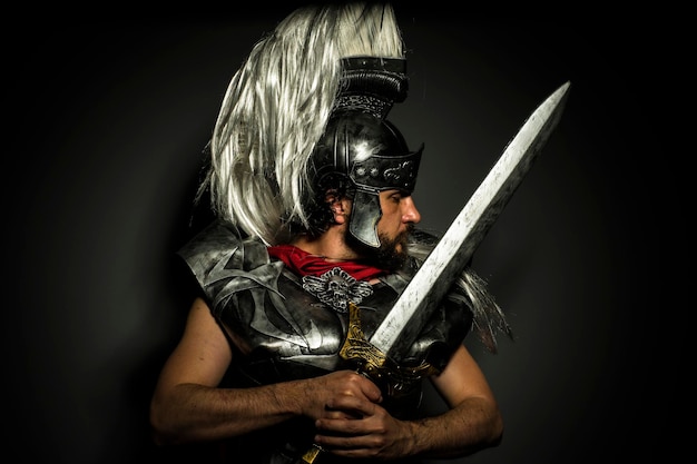 Photo empire, roman centurion with armor and helmet with white chalk, steel sword and long red cape