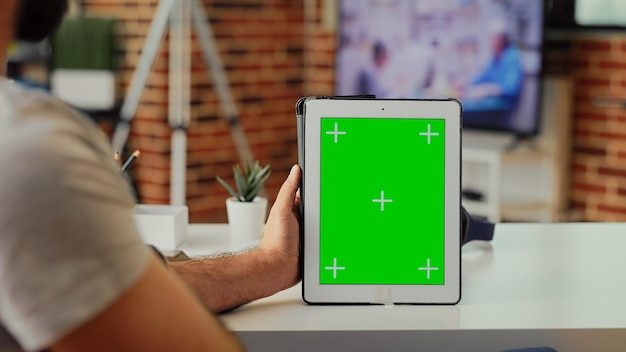 격리된 크로마 키 카피스페이스 템플릿이 있는 디지털 장치를 들고 집에 있는 최신 태블릿에서 그린스크린을 분석하는 직원. 휴대용 가젯에서 빈 모형 배경을 보고 있습니다.