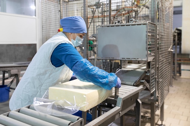 An employee in a blue form packs a large piece of oil into a transparent film on the production line The production process at the dairy plant