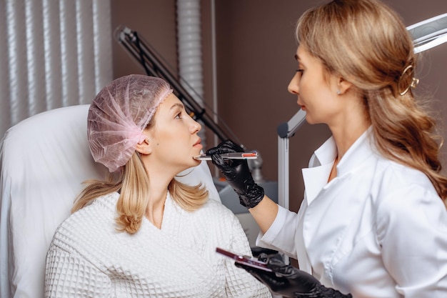 An employee in the field of cosmetology puts markings on the face of a young girl for a rejuvenation procedure