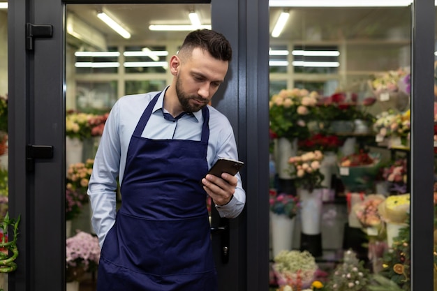 Un impiegato di un negozio di fiori in assenza di un cliente ammazza il tempo guardando il telefono