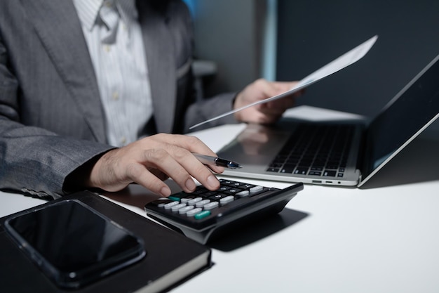 Photo an employee is seriously calculating numbers in an important document a calculator is used by a young businessman to calculate the total profit within the second quarter