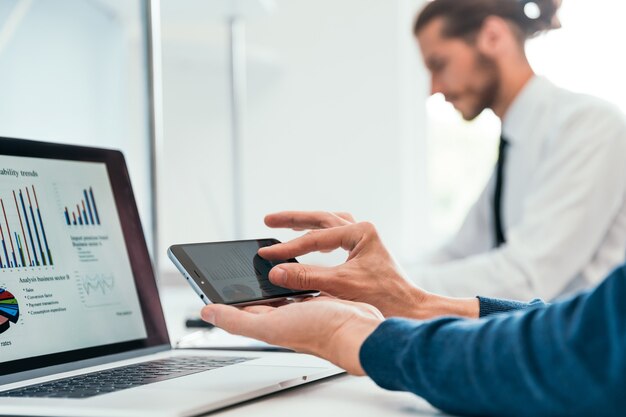 Employee is using his smartphone to check the financial data