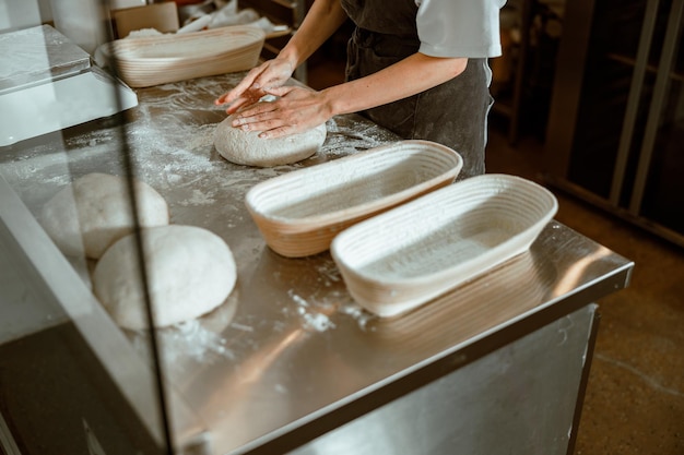 Photo employee kneads dough for bread at table with dishes in craft bakery