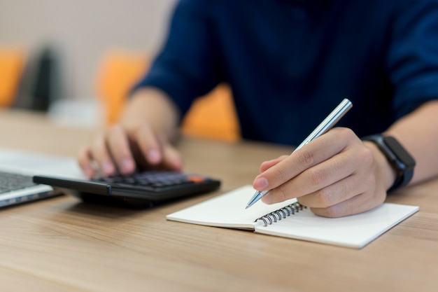 employee man hand writing on notebook and press on calculator