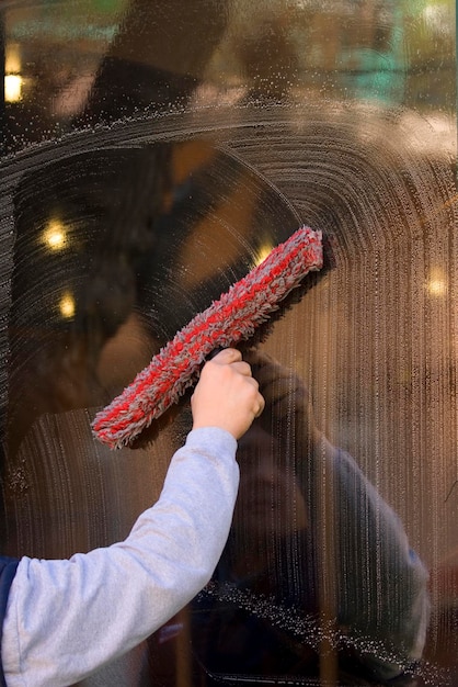 An employee of a professional cleaning service in overalls washes the glass of the windows of the facade of the building Showcase cleaning for shops and businesses