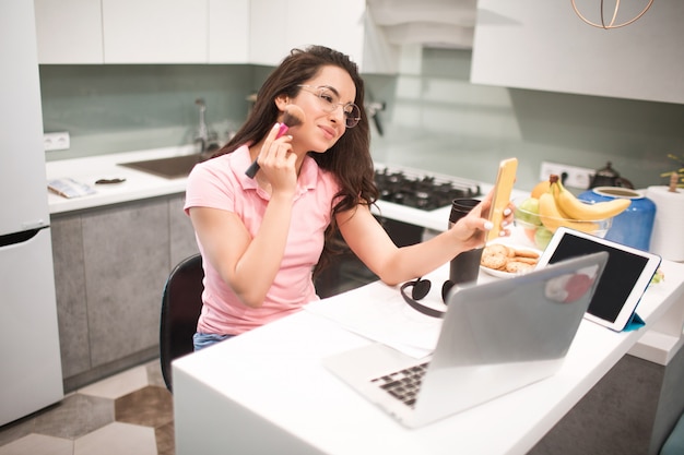 An employee sits in the kitchen and makes a make-up before an online conference