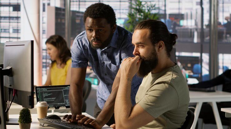 Photo employee using computer to analyze datasets being assisted by helpful coworker