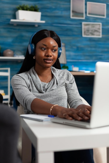 Employee working on business project with laptop and headset at home. Young woman using headphones and modern device with technology, doing online remote work and listening to music.