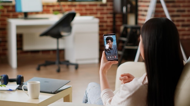 Dipendente che lavora in remoto da casa mentre parla con un collega in videoconferenza online virtuale. giovane donna adulta che discute con il collega di lavoro in videochiamata digitale tramite telefono.