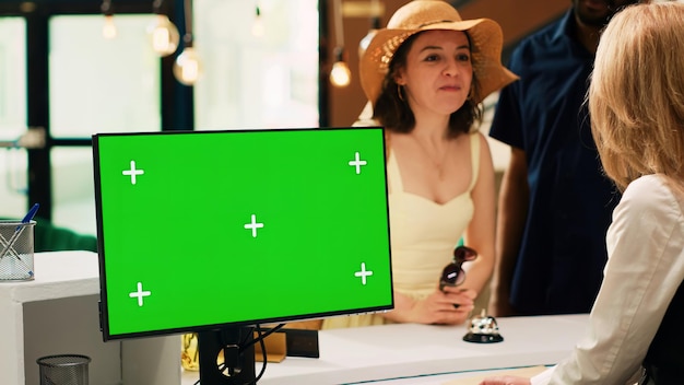 Employee working with greenscreen at hotel front desk talking to guests at reception Receptionist using isolated copyspace display with chroma key template doing check in process