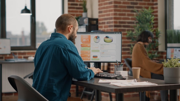 Employee working with rate data charts on computer at desk. Business man using technology to design analysis information and plan marketing project. Concentrated entrepreneur at work