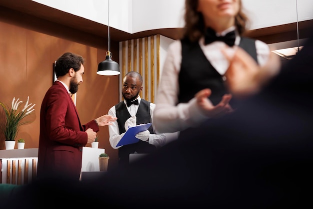 Foto dipendente che scrive le informazioni sugli ospiti per la procedura di check-in, fornendo assistenza per una facile registrazione. colletto bianco che discute con il concierge dell'hotel sulla prenotazione della camera e saluta il viaggiatore.