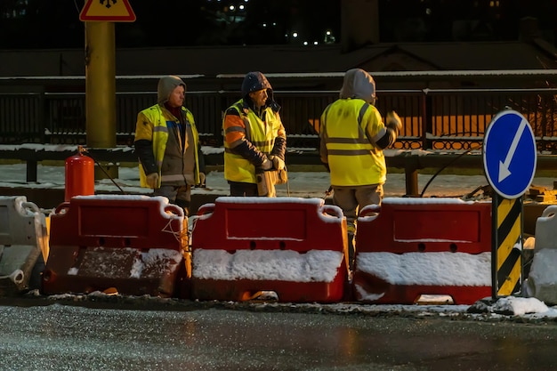 Employees of the road service in special yellow vests perform\
work on the repair of the roadway night road repairs in difficult\
winter conditions during severe frosts