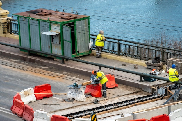 Employees of the road service in special yellow vests perform\
work on the repair of the roadway restoration of the deformation\
seam of the automobile bridge