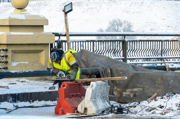 Employees of the road service in special yellow vests perform\
work on the repair of the roadway restoration of the deformation\
seam of the automobile bridge
