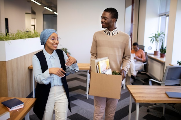 Employer showing man his desk at new job while carrying box of belongings