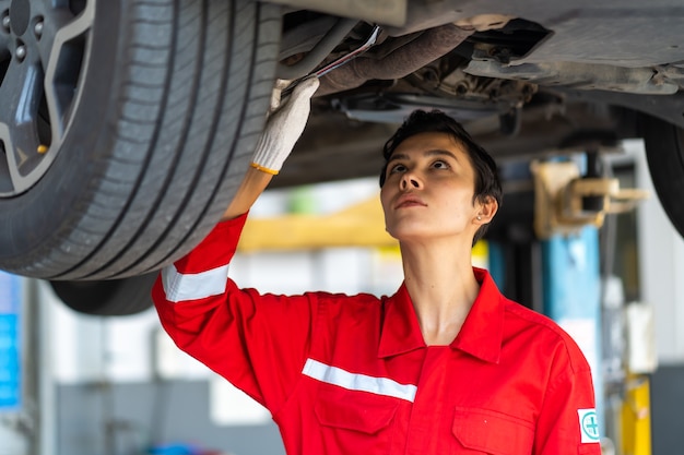 Empowering caucasian waman mechanic wearing red uniform working Under a Vehicle in a Car Service station