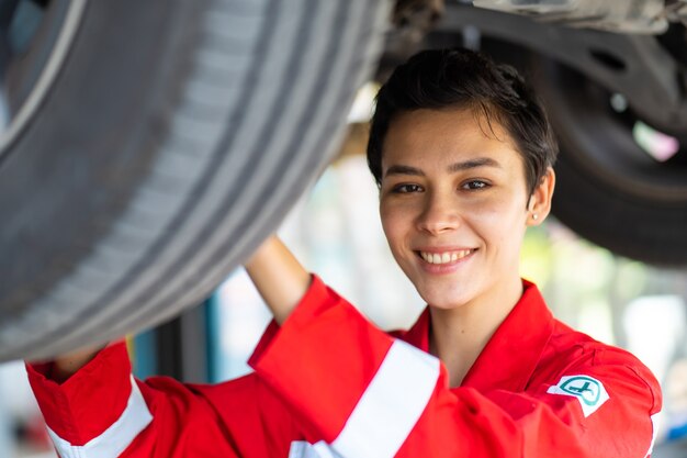 Empowering caucasian waman mechanic wearing red uniform working Under a Vehicle in a Car Service station