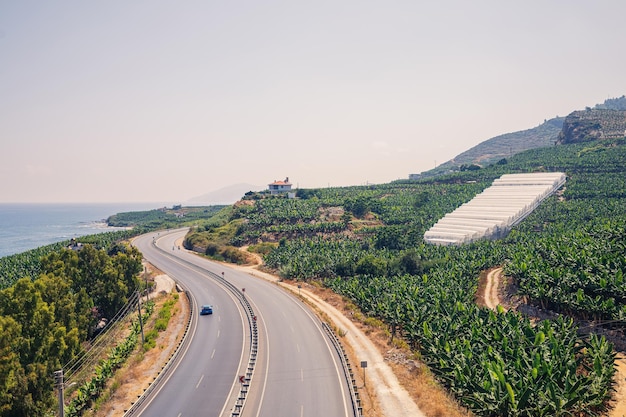 An empty asphalt road winds along the breathtaking scenic coastline on a sunny summer day A spectacular shot of a coastal road overlooking clear blue skies and the calm Mediterranean Sea