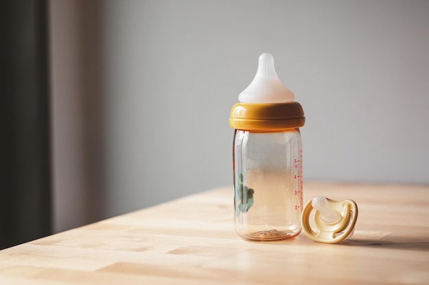 Empty baby milk bottle and pacifier on wooden table