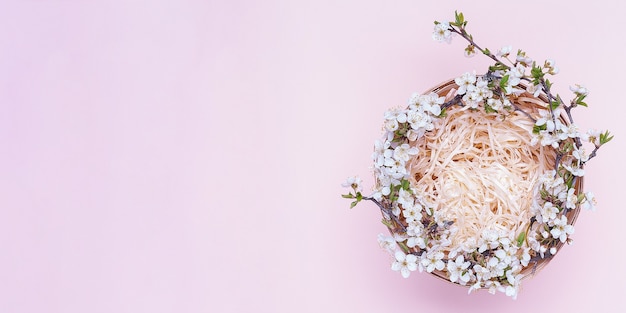 Empty basket with a wreath of white flowers on a pink background.