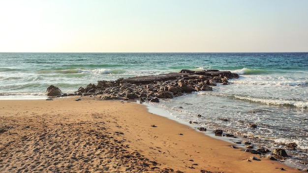 Empty beach with footsteps, some rocks in sea, in evening few moments before sunset. Lapta, Northern Cyprus