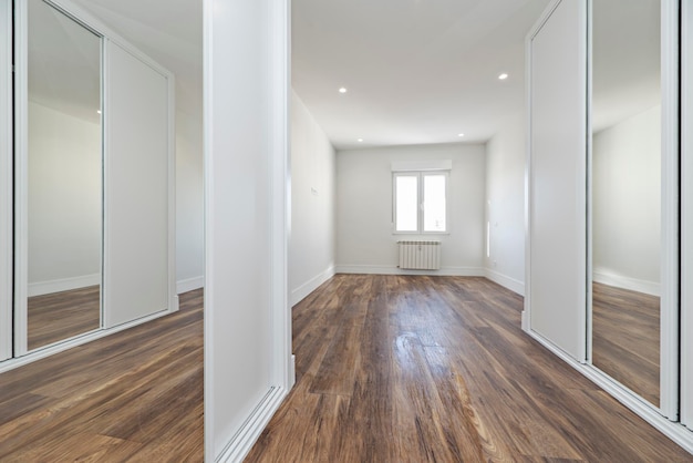 Empty bedroom with fitted wardrobes with wooden sliding doors and a mirror with wooden floors