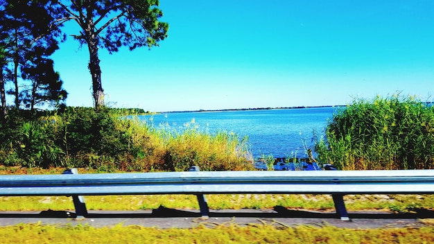 Photo empty bench by calm lake against clear blue sky