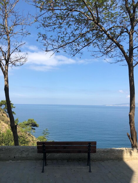 Empty bench by sea against sky