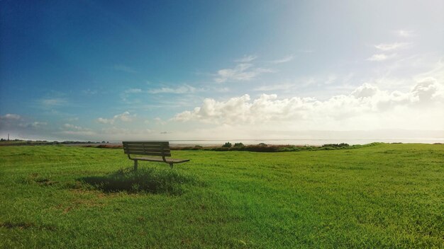 Empty bench on field against sky