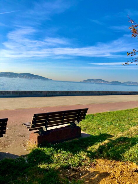 Empty bench on shore against sky