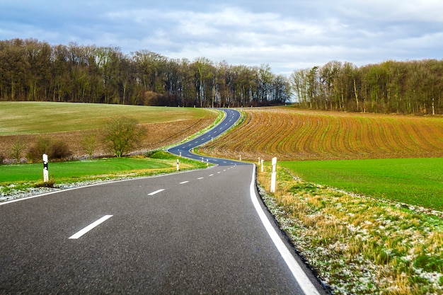 Empty black asphalt road between green fields