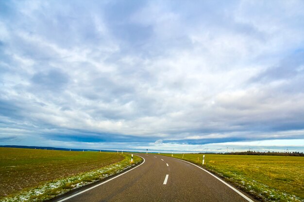 Empty black asphalt road between green fields