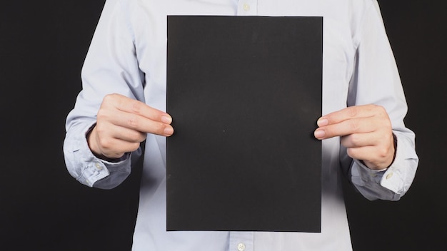 Empty black board A4 paper in man hand and wear blue shirt on black backgroundCrop body part