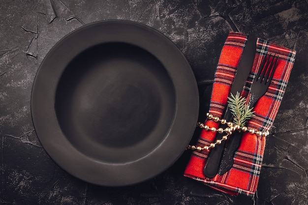 空の黒のミニマルなプレートとクリスマスの装飾が施された黒のカトラリー