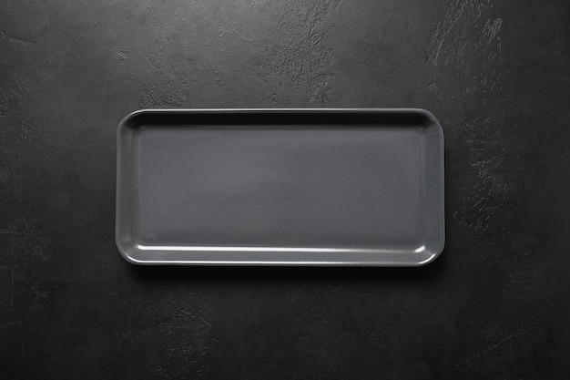 Empty black modern rectangular plate on black background, kitchen stuff, flat lay for cooking as background.