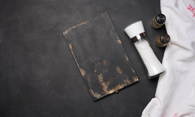 Empty black wooden board salt in a glass bottle on a black table top view