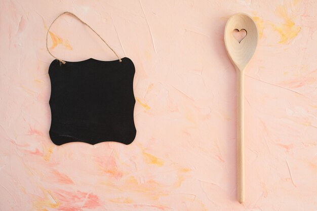 Empty blackboard and stirring spoon on a pink background