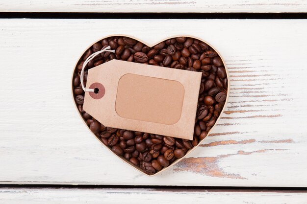 Empty blank label for copyspace lying over coffee beans. Top view flat lay. White wooden background.