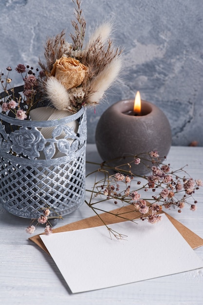 Empty blank note and kraft envelope with lit candle on white wooden table. Copy space for text, for greeting, invitation