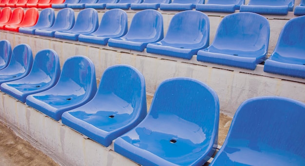 Empty bleacher in sports stadium in rainy weather Colored wet seats in street stadium It's raining Close up