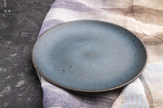 Empty blue ceramic plate on black concrete background. Side view, close up.