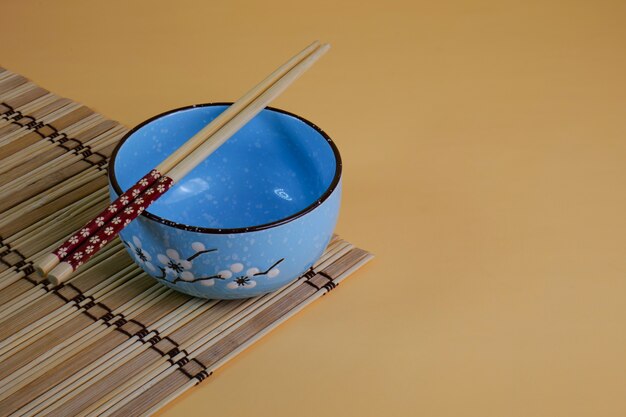 An empty blue ceramic rice bowl on a saucer with empty chopsticks on top. Ready to use