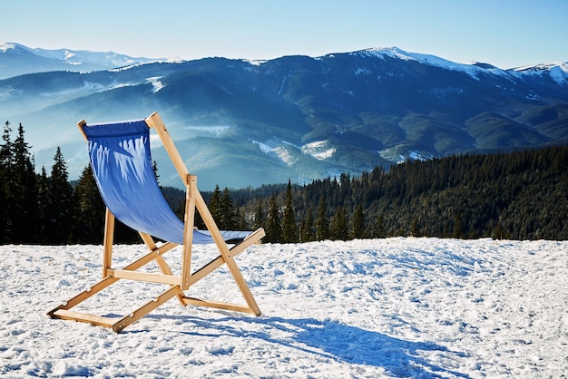 Empty blue chaise lounge, facing the snow-covered mountains