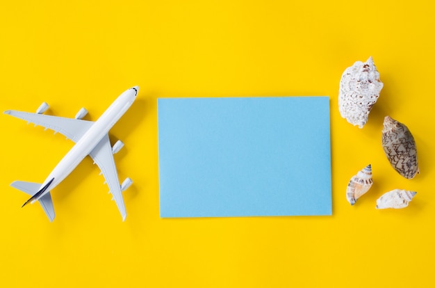 Foto svuoti la carta blu su fondo giallo con le conchiglie e l'aeroplano decorativo. concetto di viaggio estivo.