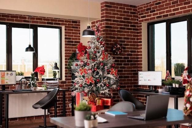 Empty business office with christmas tree decorations, festive
holiday decor and lights to celebrate winter season at startup job.
no people in company workplace filled with xmas ornaments.