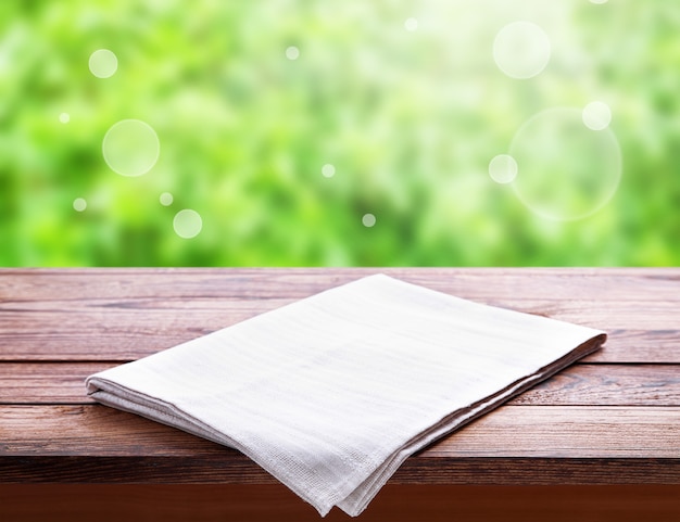 Empty canvas napkin, white tablecloth on wooden table perspective. Summer landscape.