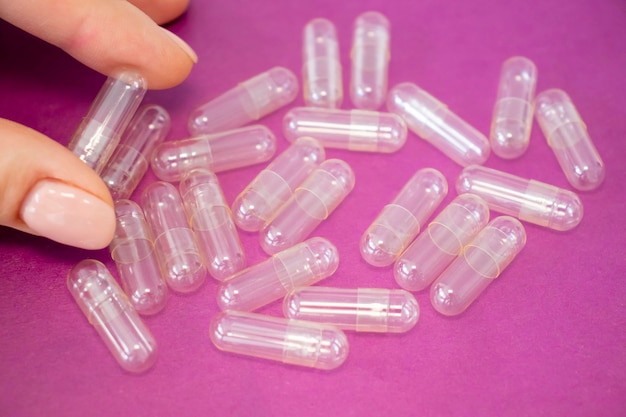 Empty capsule in a woman's hand on a pink background with empty pills